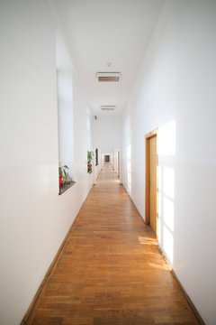 Long empty hallway inside an old building with white freshly painted walls and parquet floors