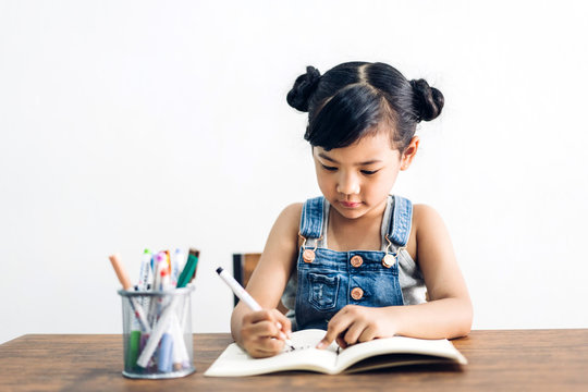 School kid little girl learning and writing in notebook with pencil making homework at home.Education concept