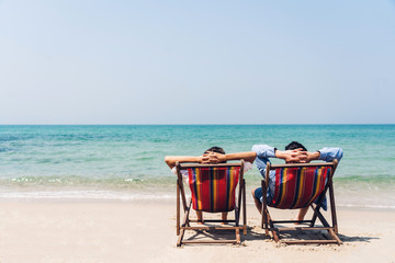 Romantic lovers young couple relaxing sitting together on the tropical beach and looking to the sea.Summer vacations