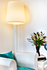 Stand lamp turned on near the blurred sofa and vase