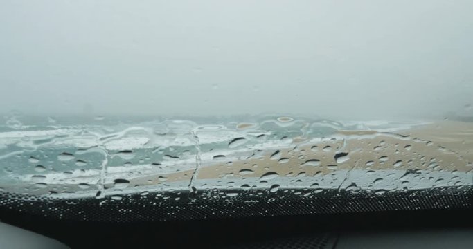 Limpador de parabrisa &eacute; acionado, atrav&eacute;s do vidro molhado se v&ecirc; uma bela praia em um dia chuvoso