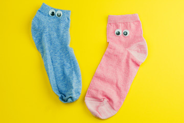 two cute pink and blue  socks with googly eyes isolated on yellow background