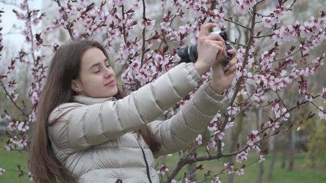 Young photographer. A cute girl takes pictures of herself against the background of flowering trees.