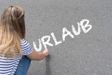 Eine Frau malt das Wort Urlaub auf die Stra&szlig;e