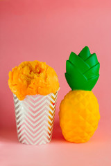 yellow fruit ice cream or frozen yogurt in stripped   cup and pineapple  on a pink background