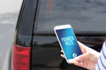 EIn Auto und Frau mit Smartphone sucht Pannenhilfe