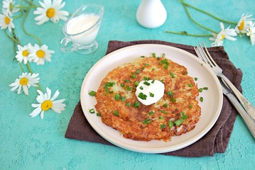 Roshty, fried potato pancake from boiled potatoes on a white clay plate on a turquoise background. Served with sour cream. Swiss cuisine.