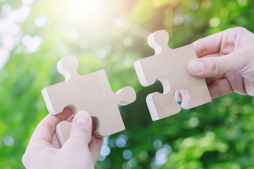 two hands person trying to connect couple Jigsaw wooden puzzle piece with tree fresh background....