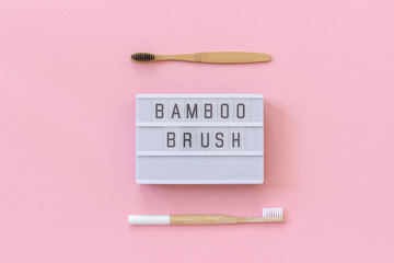 Two natural eco-friendly bamboo brushes with white and black bristles and lightbox text Bamboo brush on pink paper background. Top view Flat lay Template Concept