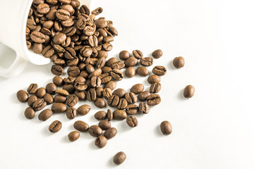 Scattered coffee beans from a cup on a white background. Pile of brown roasted coffee beans in coffee cup. Concept of freshness or great aroma and energy .