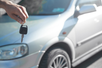 Man holding car key with car background.