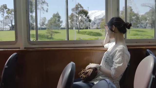 Slow motion shot of Asian tourist looking out the window of a tram on a beautiful sunny day at Melbourne, Australia