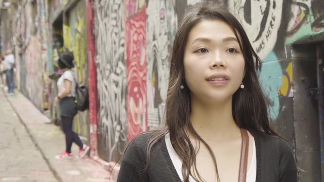 Young Asian girl looking into camera and then looking at artwork and taking a photo at Hosier Lane, Melbourne, Australia