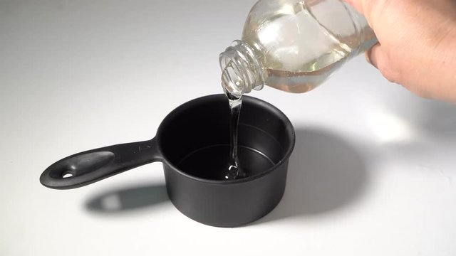 Hand pours clear fructose corn syrup into measuring cup, slow motion
