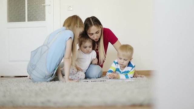 Mother with children reading a book on a gray carpet at home.