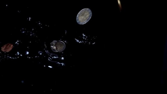 Coins fall in water. Slow motion.