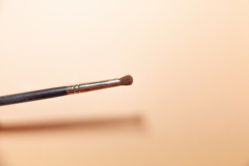 A makeup brush is pictured in front of a pink background