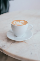 A cup of coffee with beautiful latte art in a white cup on marble table background.