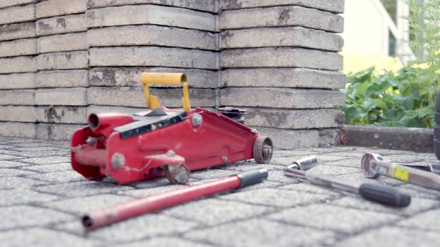 Tools lie on the ground, prepared for a tire change: A stack of wheels / tires, a wheel wrench, a normal wrench, a torque wrench and a car jack with two parts.