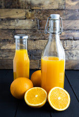 still life photo of orange juice, orange smoothie in glass bottles on wooden background.