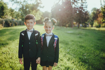 little boy and little girl, two schoolgirls look at the camera, outdoor, at sunset