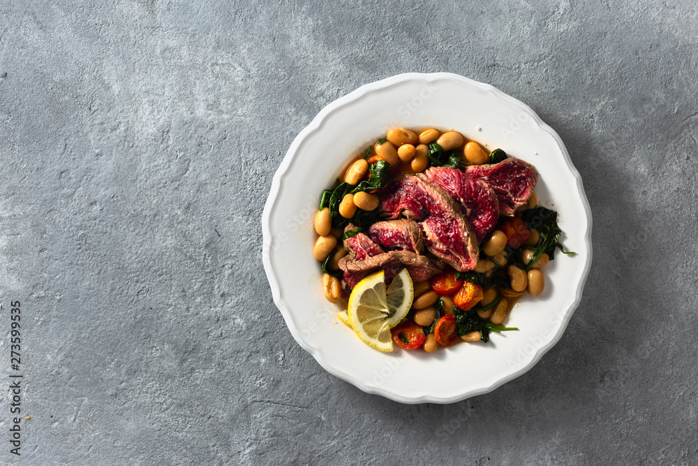 Wall mural Dinner plate with beef steak, white beans, spinach and tomatoes top view with copy space