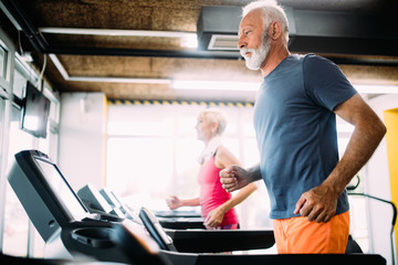 Senior people running on a treadmill in health club.