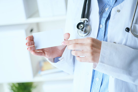 Close-up image of female doctor with stethoscope and blank visiting card with place for text in hands.