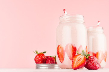 Set of two fresh cold milkshake in hipster jars with cut ripe berries, striped straws in elegance pink kitchen interior, copy space, closeup.