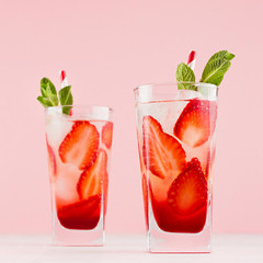 Fresh cold strawberry cocktail with green mint, ice, straw on soft light pastel pink background, square.