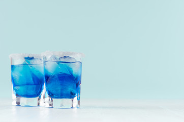 Cool summer blue beverage margarita for party with ice cubes, salt rim in two wet shot glasses on...