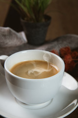 A cup of hot coffee  with coffee bean and milk cup on wooden table