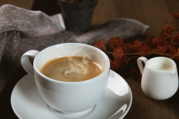 A cup of hot coffee  with coffee bean and milk cup on wooden table