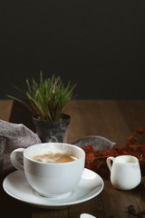 A cup of hot coffee  with coffee bean and milk cup on wooden table