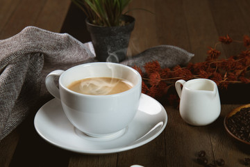 A cup of hot coffee  with coffee bean and milk cup on wooden table