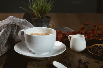 A cup of hot coffee  with coffee bean and milk cup on wooden table