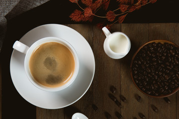 A cup of hot coffee  with coffee bean and milk cup on wooden table