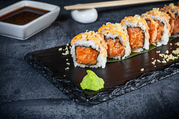 Close up view on set of sushi roll. Spicy roll with salmon and caviar served on black stone on dark background. Japanese cuisine. Copy space. Served sushi for menu. Healthy food, seafood