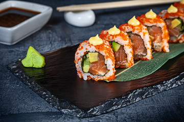 Close up view on set of sushi roll. California roll with salmon, avocado and caviar served on black stone on dark background. Japanese cuisine. Copy space. Served sushi for menu. Healthy food, seafood