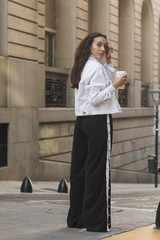 Young woman standing in front of building holding takeaway coffee cup looking over shoulder