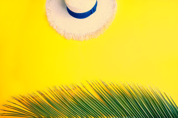 Tropical palm leaf and sun straw hat on yellow background with copy space. Concept for summer vacation concept flat lay.