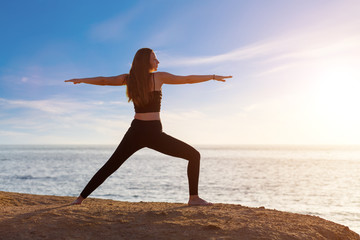 Fototapeta premium Young woman practicing yoga asana pose in the morning at the sea