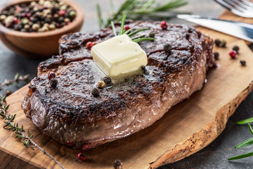 Medium rare Ribeye steak with herbs and a piece of butter on the wooden tray.
