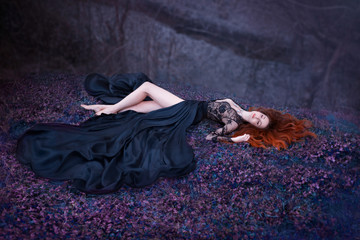 lady sleeping on the ground with long red fiery hair lies in a luxurious black lace dress with a...