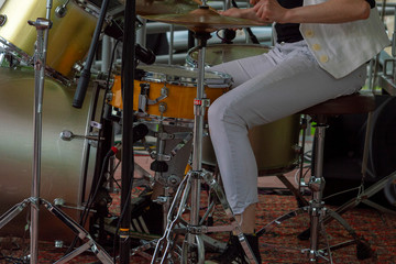 Fototapeta na wymiar Woman in white jeans and sneakers plays the drum set