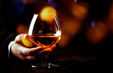 French glowing cognac glass in hand on the dark bar counter background, copy space, selective focus - obrazy, fototapety, plakaty