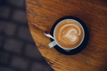 Cappuccino cup with heart shaped latte art standing on a wooden table