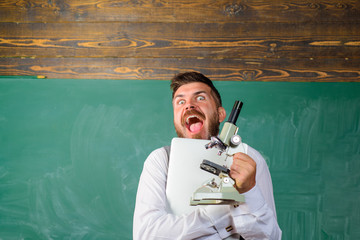 Happy scientist with laptop and microscope. Bearded man with notebook and microscope. College teacher with computer and microscope. Research concept. Excited tutor in classroom. Educational theme.