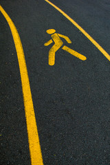 Yellow walking trail symbol on black asphalt road