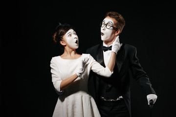 portrait of surprised couple mime on black background. man in tuxedo and glasses and woman in white dress